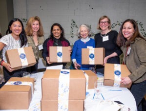 Women holding and standing with Hand in Hand care packages they assembled.